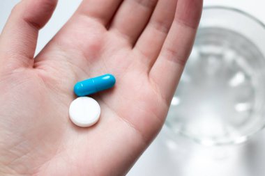 Kadın avucunda mavi ve beyaz hap kapsülü var. Kadın elinde antidepresan haplar. Avucunda bir bardak suyla hap tutan bir kadın.