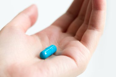 Beyaz arka planda dişi avucunda mavi hap kapsülü var. Kadın sağlığı için besin takviyesi. Avucunun içinde hap tutan bir kadın.