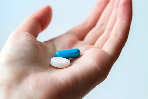 Blue and white pill capsule on the female palm on white background. Antidepressant pills in female hand. Female hand holding a pill on the palm