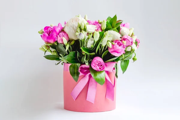 Arrangement of flowers in a hat box. Bouquet of pink and white peonies, eustoma, spray rose in a pink box with an oasis on a white background with copy space