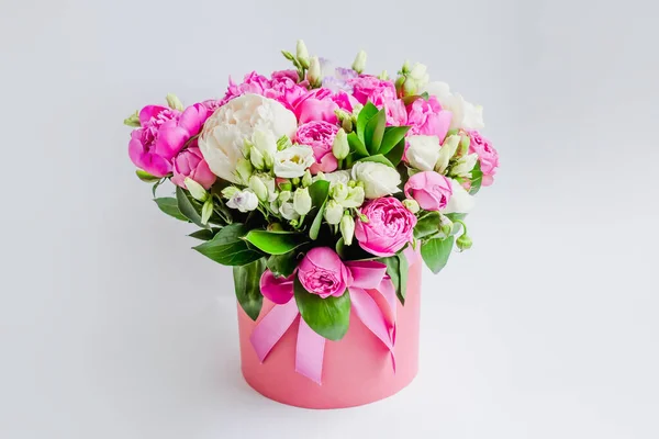 Arrangement of flowers in a hat box. Bouquet of peonies, eustoma, spray rose in a pink box with an oasis on a white background