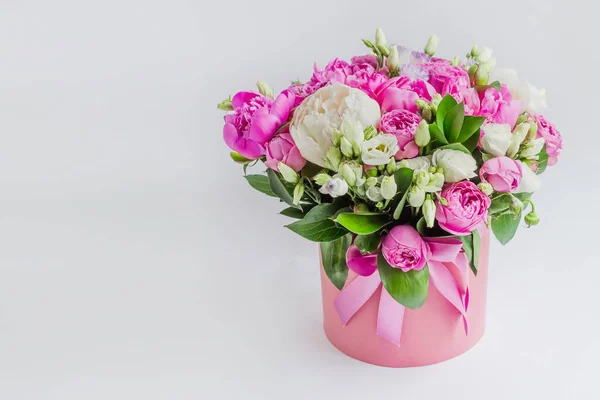 Arrangement of flowers in a hat box. Bouquet of peonies, eustoma, spray rose in a pink box with an oasis on a white background