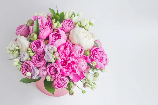 Arrangement of flowers in a hat box. Bouquet of peonies, eustoma, spray rose in a pink box with an oasis on a white background with copy space