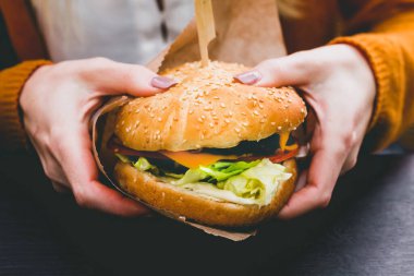 Siyah ahşap masada patates kızartması ve taze lezzetli bir burger tutan kadın eller.