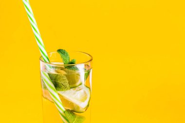 Taze yaz limonatası, su, limon ve nane şekerli ve sarı arka planda pipetli. Soğuk, ferahlatıcı yaz kokteyli yakın çekim. Fotokopi alanı olan taze içecek