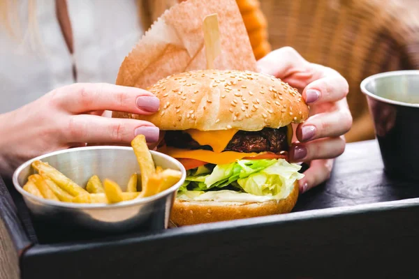 Hands holding fresh delicious burger with french fries on the black wooden table