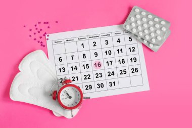 Regl takvimi, çalar saat, hormonal doğum kontrol hapları. Kadınların adet döngüsü konsepti. Adet sancıları için ağrı kesici.