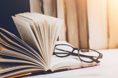 Ahşap bir masanın üzerindeki gözlüklü açık bir kitap. Arka plandaki kitaplara karşı, klasik tonlama. Edebiyat, öğrenme konsepti