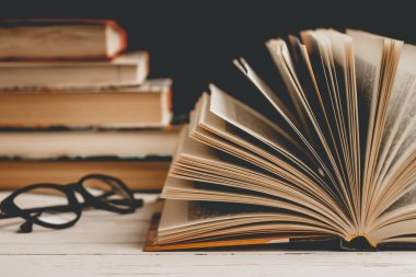 Ahşap bir masanın üzerindeki gözlüklü açık bir kitap. Arka plandaki kitaplara karşı, klasik tonlama. Edebiyat, öğrenme konsepti