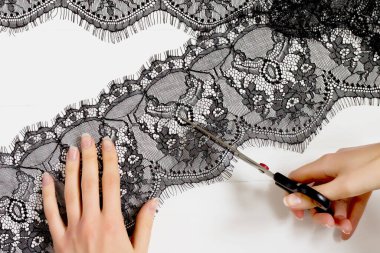 Kadın eli, bir makasla kesilir beyaz ahşap arka planda siyah bir dantel parçası. Elbiseler, elbiseler için dekorasyon. Terzi, dantelli bir gece elbisesi diker.