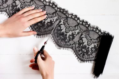 Kadın eli, bir makasla kesilir beyaz ahşap arka planda siyah bir dantel parçası. Elbiseler, elbiseler için dekorasyon. Terzi, dantelli bir gece elbisesi diker.