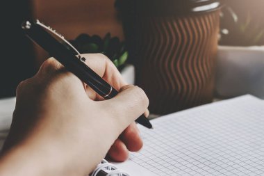 Kadın bir kalem tutuyor ve bir deftere yazıyor, koyu arkaplan. Solak kız not defterine notlar alır, koyu tonlu fotoğraf.