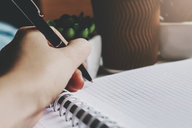 Kadın bir kalem tutuyor ve bir deftere yazıyor, koyu arkaplan. Solak kız not defterine notlar alır, koyu tonlu fotoğraf.