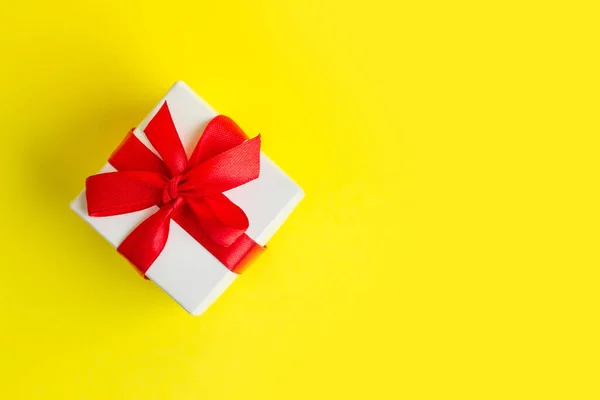 White box with a red ribbon on a yellow background, copy space. Greeting card concept. Gift concept