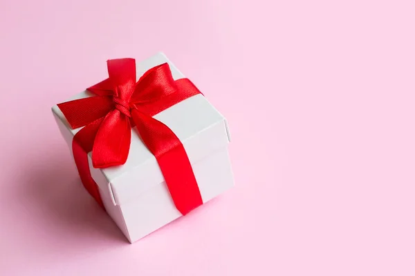 White box with a red ribbon on a light pink background, copy space. Greeting card concept. Gift concept
