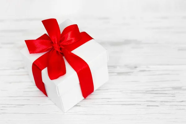 White gift box with a red ribbon on a white wooden background, copy space. Greeting card concept. Gift concept