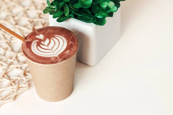 Cup of cappuccino in a paper cup with a pattern on a table in a cafe, copy space