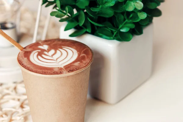 Cup of cappuccino in a paper cup with a pattern on a table in a cafe