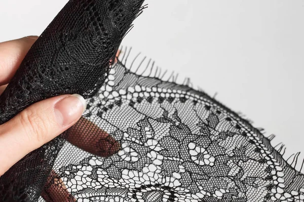 Female hand holds black lace on gray background. Lace with floral ornaments
