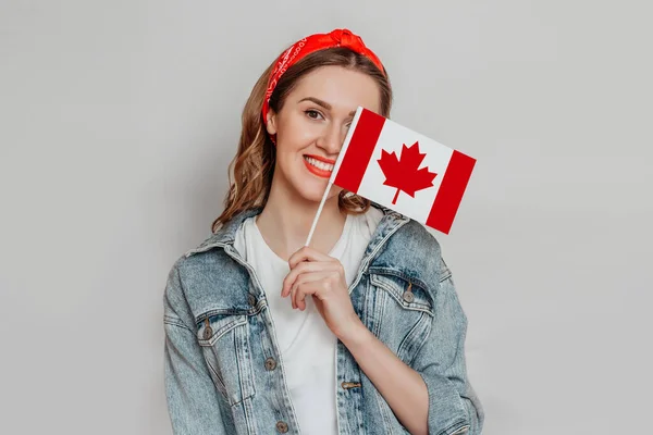 Female student smiling and cover half of her face with a small canada flag isolated over white background, Canada day, holiday, confederation anniversary, copy space