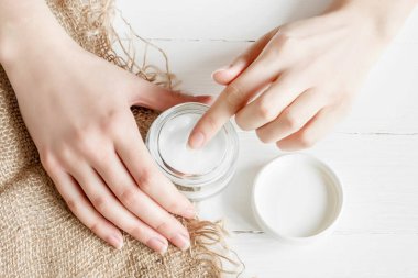 Beyaz arka planda krema kavanozu olan bir kadın eli. Kız ellerine nemlendirici sürüyor. Kuru çiçek yaprakları, üst manzara. Ekolojik, doğal parfümsüz krem, doğal el bakımı yağı..