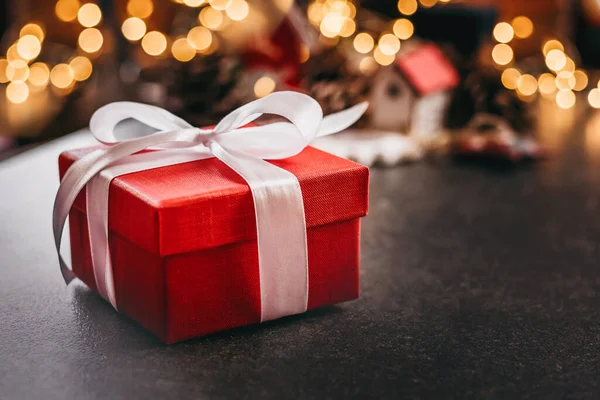 Red christmas square box with gift with white ribbon on table against bokeh background. ??py space