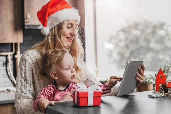 New Year\'s family video calls. Mother with a son wearing a festive hat is sitting at home with New Year\'s winter decorations calling by videoconference. Distance video chat for coronavirus quarantine