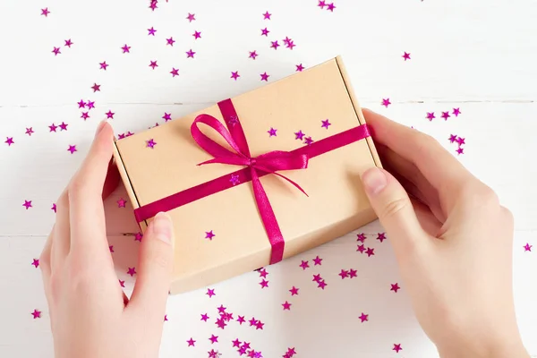 Girl opens a craft gift box on a white wooden background, top view. Gift wrapping in female hands, gift box, open present