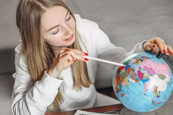Young blonde woman is studying the globe at home and points her finger at the mainland. Study of geography