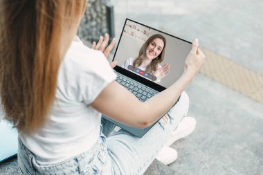 Laptop modeli. Genç kız, beyaz ekranlı dizüstü bilgisayar kullanıyor, merdivenlerde oturuyor ve ofis binasının yakınındaki boş siyah ekrana bakıyor. Tasarım için alanı kopyala