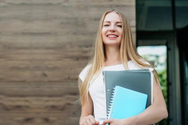 Kafkas öğrenci kız dosyaları, defterleri elinde tutuyor ve üniversite binasının arka planında gülümsüyor. Boşluğu kopyala