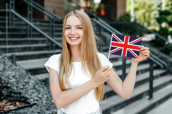 Education abroad. Female student holds a small UK British England flag and stands near the university on the street