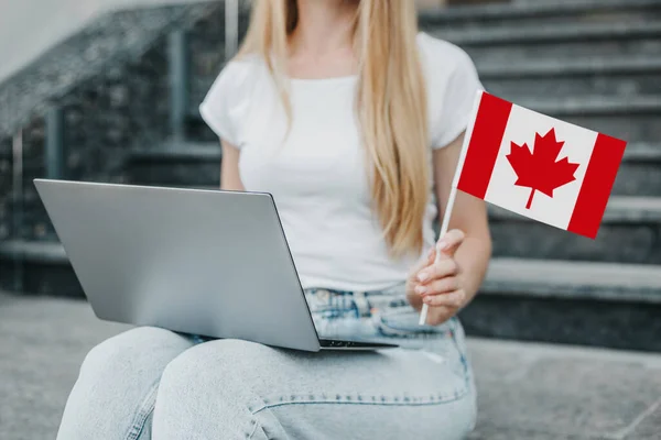 在大学的背景下 一只女手拿着一面小加拿大国旗和一台笔记本电脑 靠近点 — 图库照片