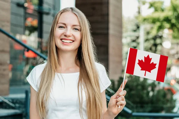 education abroad. female student shows a small canadian flag and stands against the background of the university and smiling