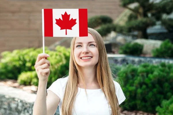 女学生看着小加拿大国旗 站在大学的背景下微笑着 — 图库照片