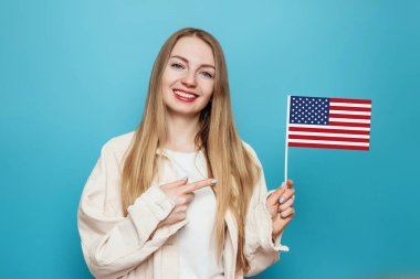Mutlu genç sarışın kadın küçük bir Amerikan bayrağını tutuyor ve mavi arka planda izole edilmiş bir şekilde gülümsüyor, elinde ABD bayrağı tutan kız, 4 Temmuz Bağımsızlık Günü, kopyalama alanı