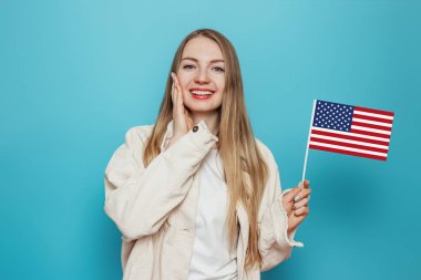 Mutlu sarışın öğrenci elinde küçük bir Amerikan bayrağı, mavi arka planda izole edilmiş bir gülümseme, elinde ABD bayrağı tutan bir kız, 4 Temmuz Bağımsızlık Günü, kopyalama alanı
