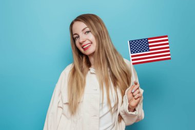 Kafkas genç sarışın kız elinde küçük bir Amerikan bayrağı, mavi arka planda saklanmış bir gülümseme, ABD bayrağı tutan bir kız, 4 Temmuz Bağımsızlık Günü, kopyalama alanı