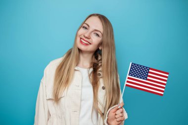 Neşeli genç sarışın kız elinde küçük bir Amerikan bayrağı, mavi arka planda saklanmış gülümsemeler, Amerikan bayrağı tutan kız, 4 Temmuz Bağımsızlık Günü, kopyalama alanı