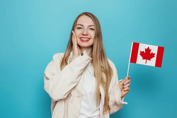 惊讶的女生笑着举着小加拿大国旗 望着蓝色背景下的相机 加拿大日 邦联周年纪念日 复制空间 — 图库照片