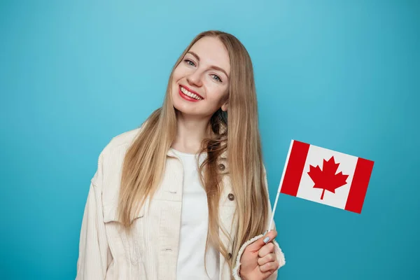 白人女学生笑着举着小加拿大国旗 望着蓝色背景下的相机 加拿大日 邦联周年纪念日 复制空间 — 图库照片