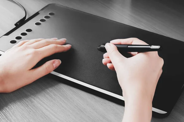 Female hands draw on a graphic tablet. Designer hand holds a pen and draws on a tablet