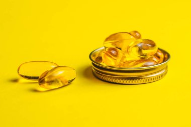 Sarı kapsüller, tabletler, balık yağı hapları sarı arka planda yatıyor. Vitamin kompleksi Omega 3,6,9. Sağlıklı gıda takviyesi