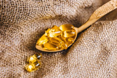 Tahta kaşıkta balık yağı kapsülleri. Balık yağı hapları, çuval bezinde haplar. Vitamin kompleksi Omega 3,6,9. Omega-3 'lü balık yağı kapsülleri, D vitamini manzaralı. Boşluğu kopyala