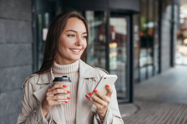 Bir ofis binasının arka planında elinde akıllı telefon ve bir fincan kahveyle gülümseyen esmer bir kadın vardı ve başka tarafa bakıyordu. Boşluğu kopyala