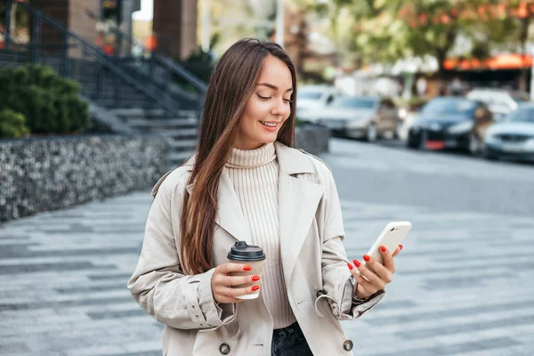 young woman uses satellite internet. A student girl sits on a bench with a mobile phone and smiles against the background of an office building