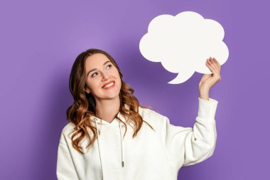 Beyaz kapüşonlu kız çocuğu elinde tuttuğu ve mor arka planda izole edilmiş kağıt kart konuşma balonuna bakıyor.