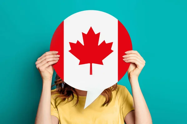girl holds blank white speech bubble with canadian flag isolated on blue background. Invitation to study in Canada concept