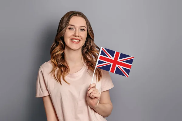 Education abroad. Female student holds a small British flag isolated over grey background. student exchange
