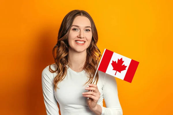 学生交流 年轻的女学生拿着一面小加拿大国旗 在橙色背景下隔离开来 加拿大日 邦联周年纪念日 复制空间 — 图库照片